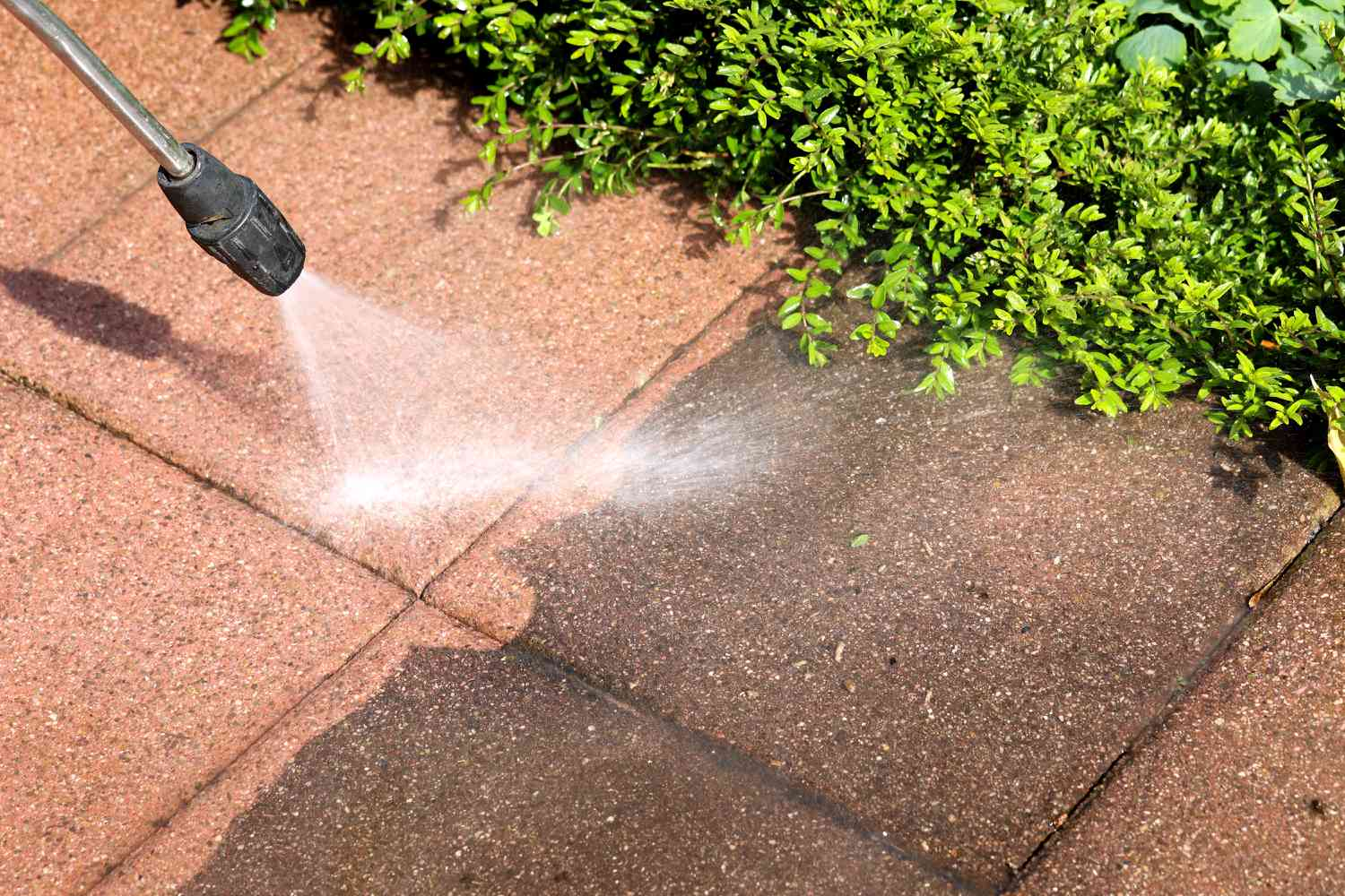Technician in a blue company shirt pressure washing a residential driveway